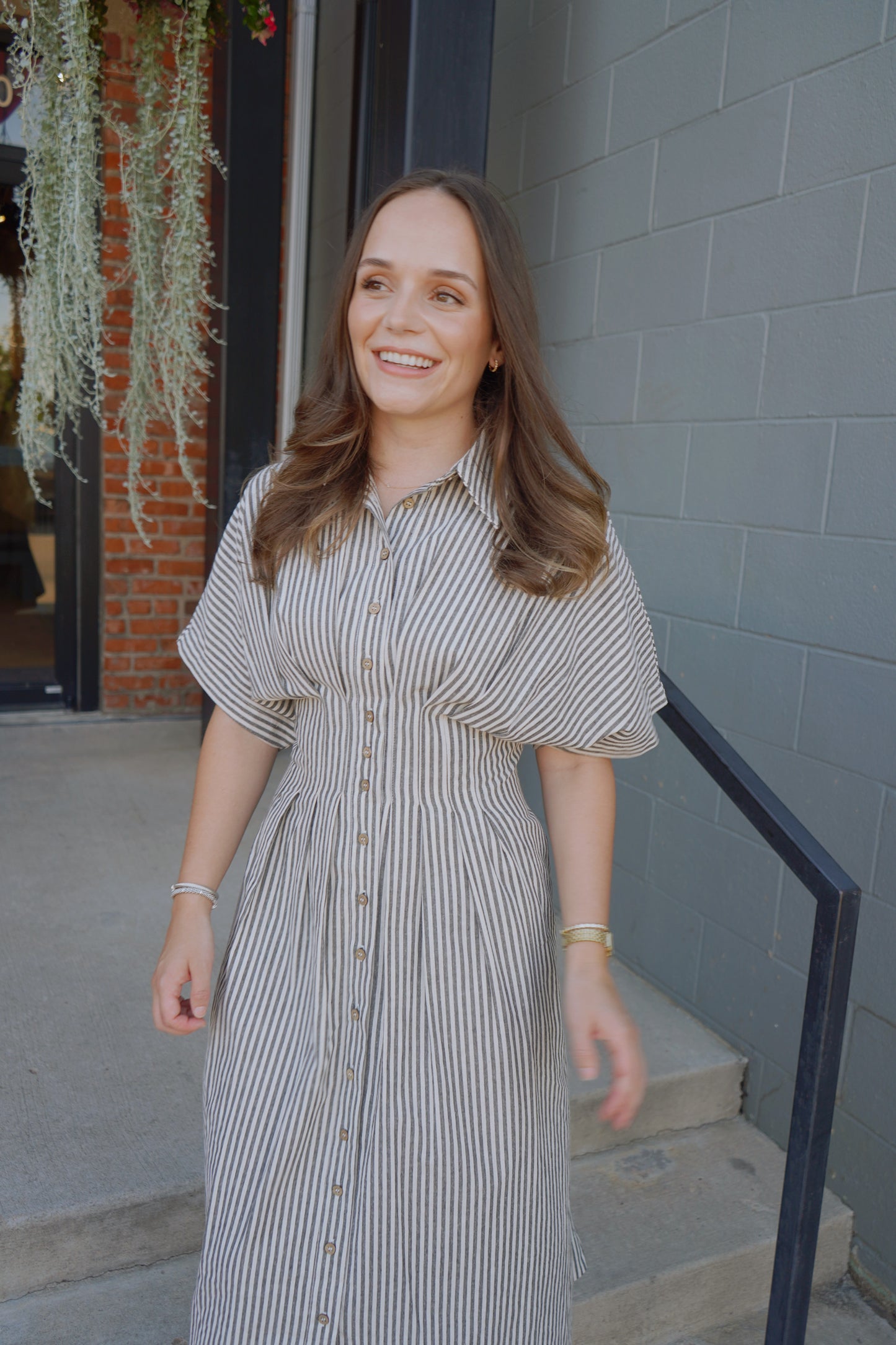 Woman in a striped dress standing outdoors against a gray wall.